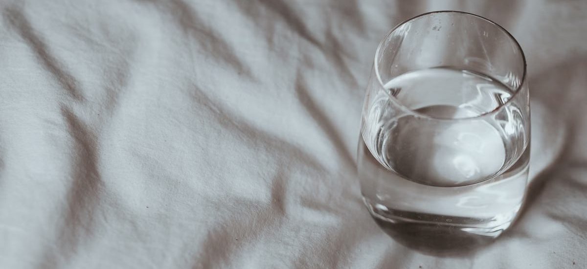 Minimalistic shot of a glass of water resting on a white duvet, taken indoors.