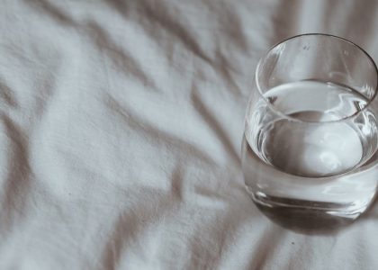 Minimalistic shot of a glass of water resting on a white duvet, taken indoors.